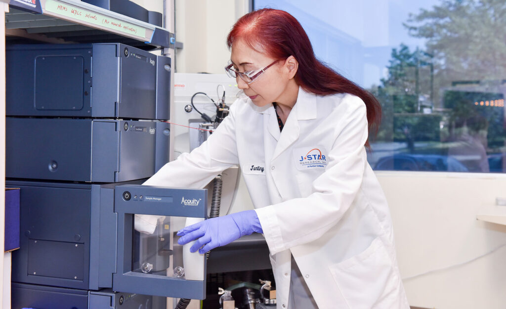Scientist in a lab coat operates a piece of laboratory equipment while wearing purple gloves.