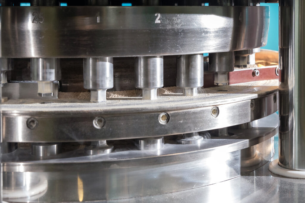 Close-up of an industrial machine pressing circular tablets from powder on a rotating plate.