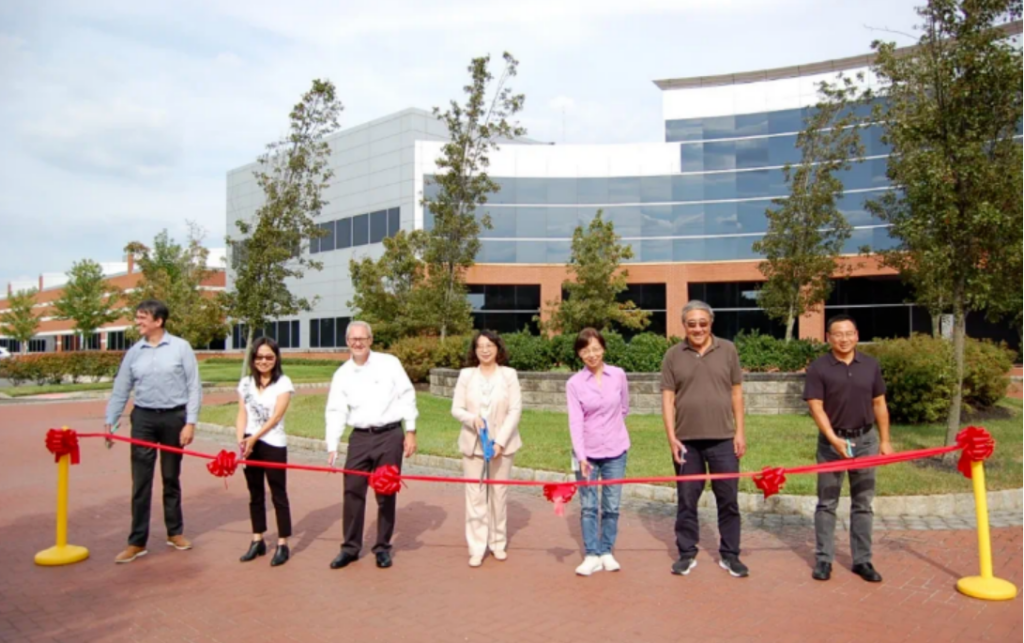 Seven people standing behind a red ribbon in front of a modern building, possibly for a ribbon-cutting ceremony.