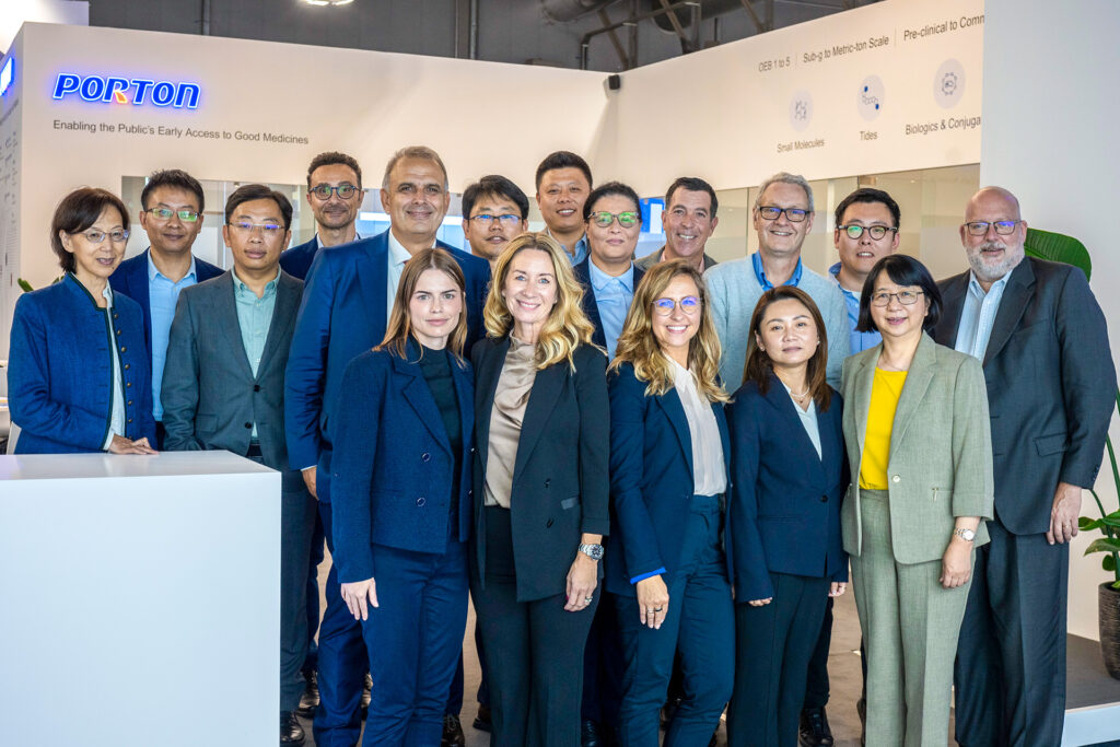 A group of 17 individuals in formal attire poses indoors against a white backdrop, with "PORTON" prominently displayed behind them. This gathering highlights Porton Pharma Solutions' commitment to excellence in the CDMO industry during the CPHI Europe Review.